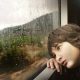 A boy staring out a train window while it rained